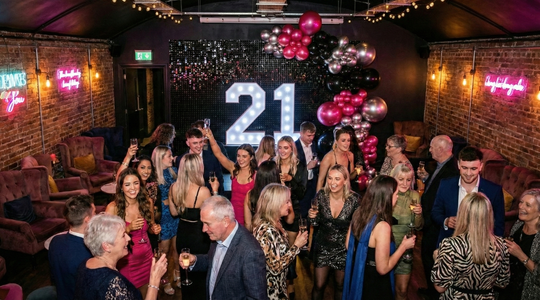 Guests celebrating a 21st birthday with Ace Party light up numbers, balloon décor and black sequin backdrop