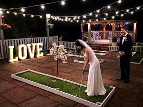 Bride and groom playing wedding crazy golf beside illuminated LOVE letters under festoon lights, South Yorkshire