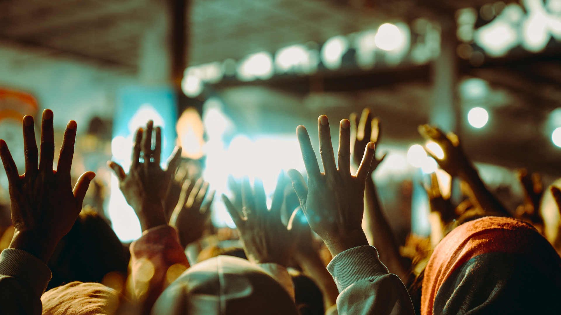 Crowd with raised hands at a concert, bright stage lights glowing in the background