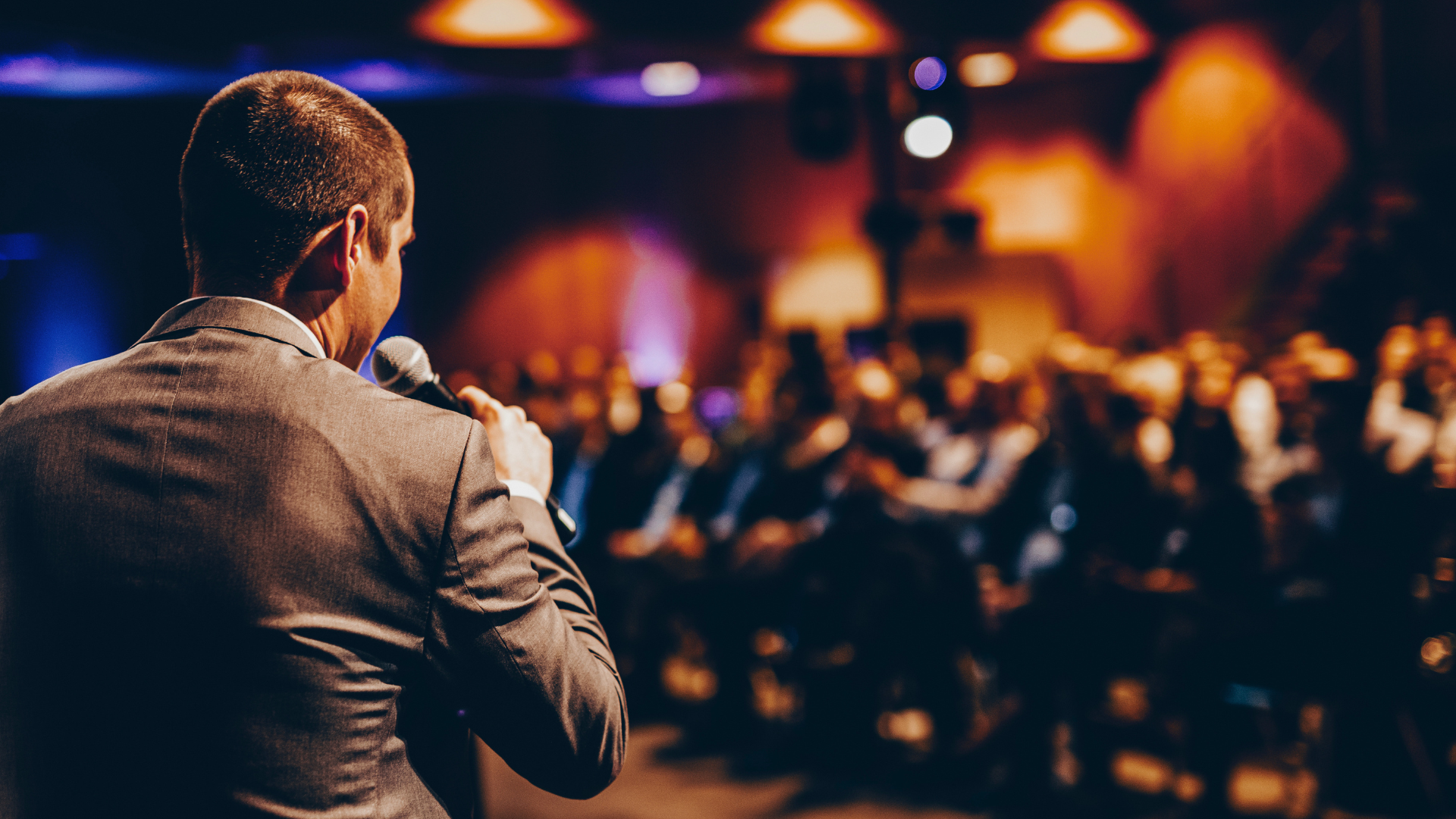 Speaker addressing a blurred audience in a warmly lit conference hall