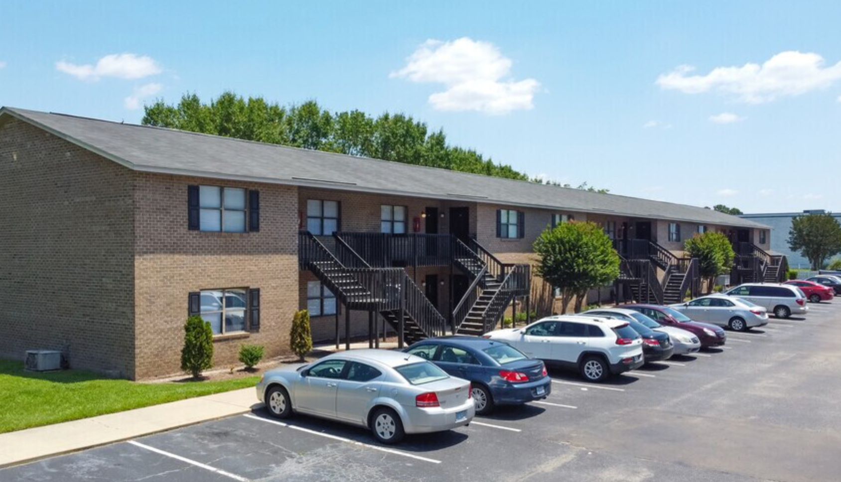 A row of cars are parked in front of a brick apartment building.