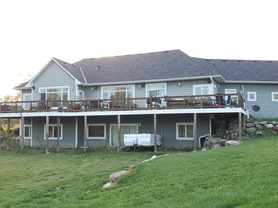 Large gray house with a raised deck and carport, set on a grassy slope at sunset