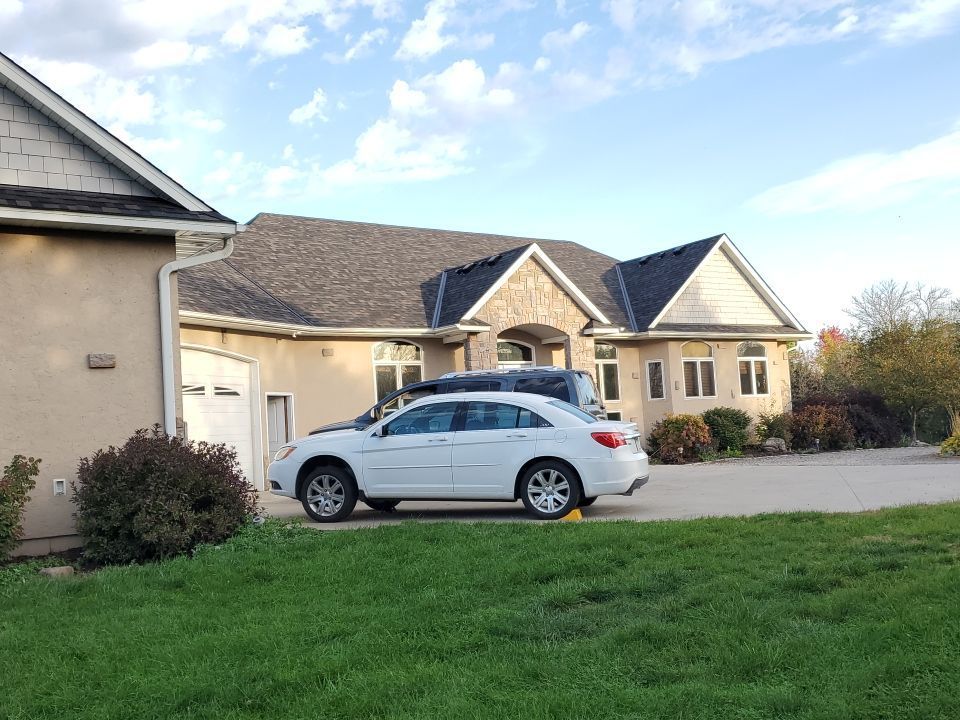 White SUV parked in front of a beige suburban house with a green lawn and blue sky