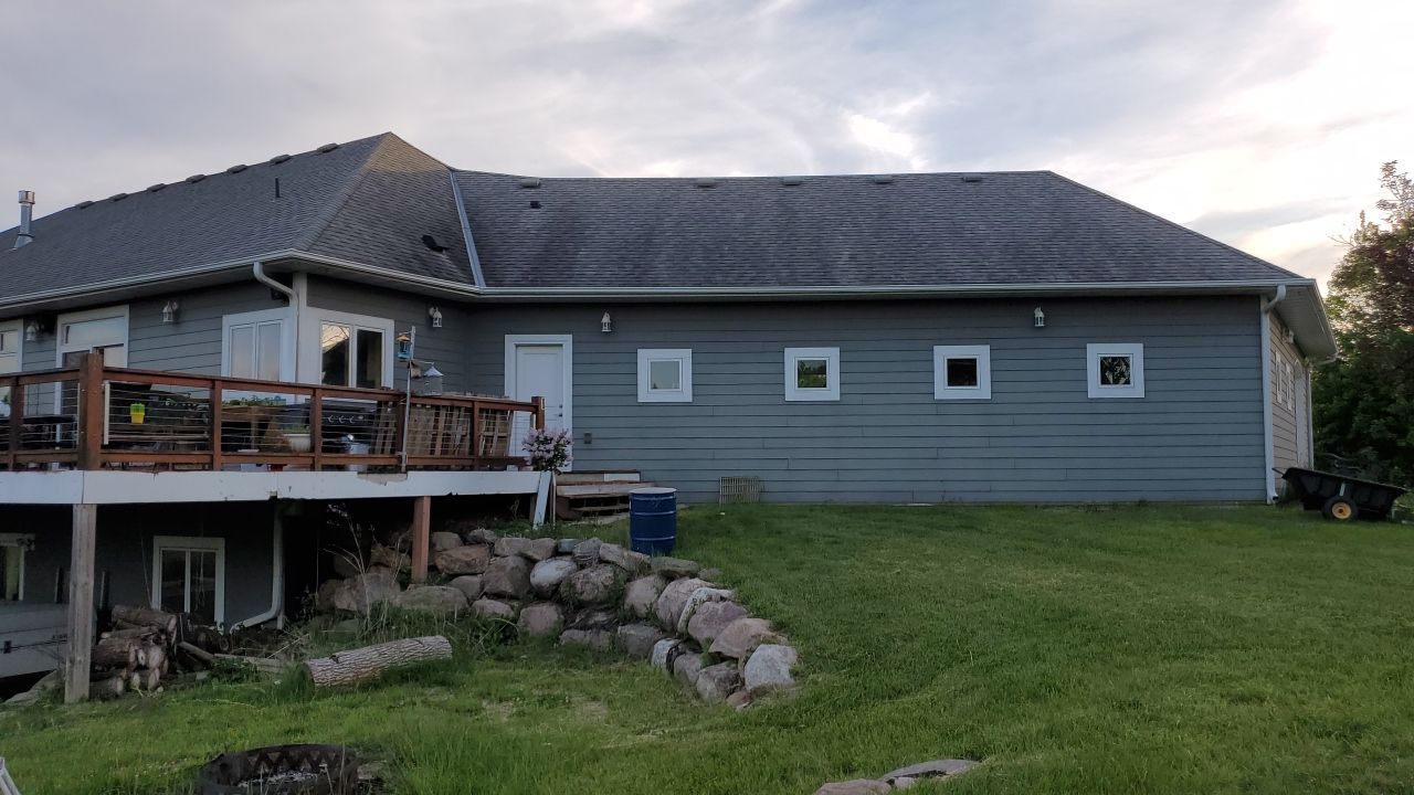 Gray house with a dark roof, wooden deck, and green lawn at dusk