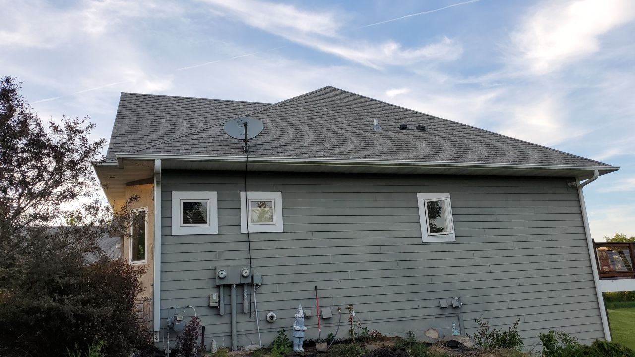 Gray house exterior with shingled roof, small windows, and utility meters on the side