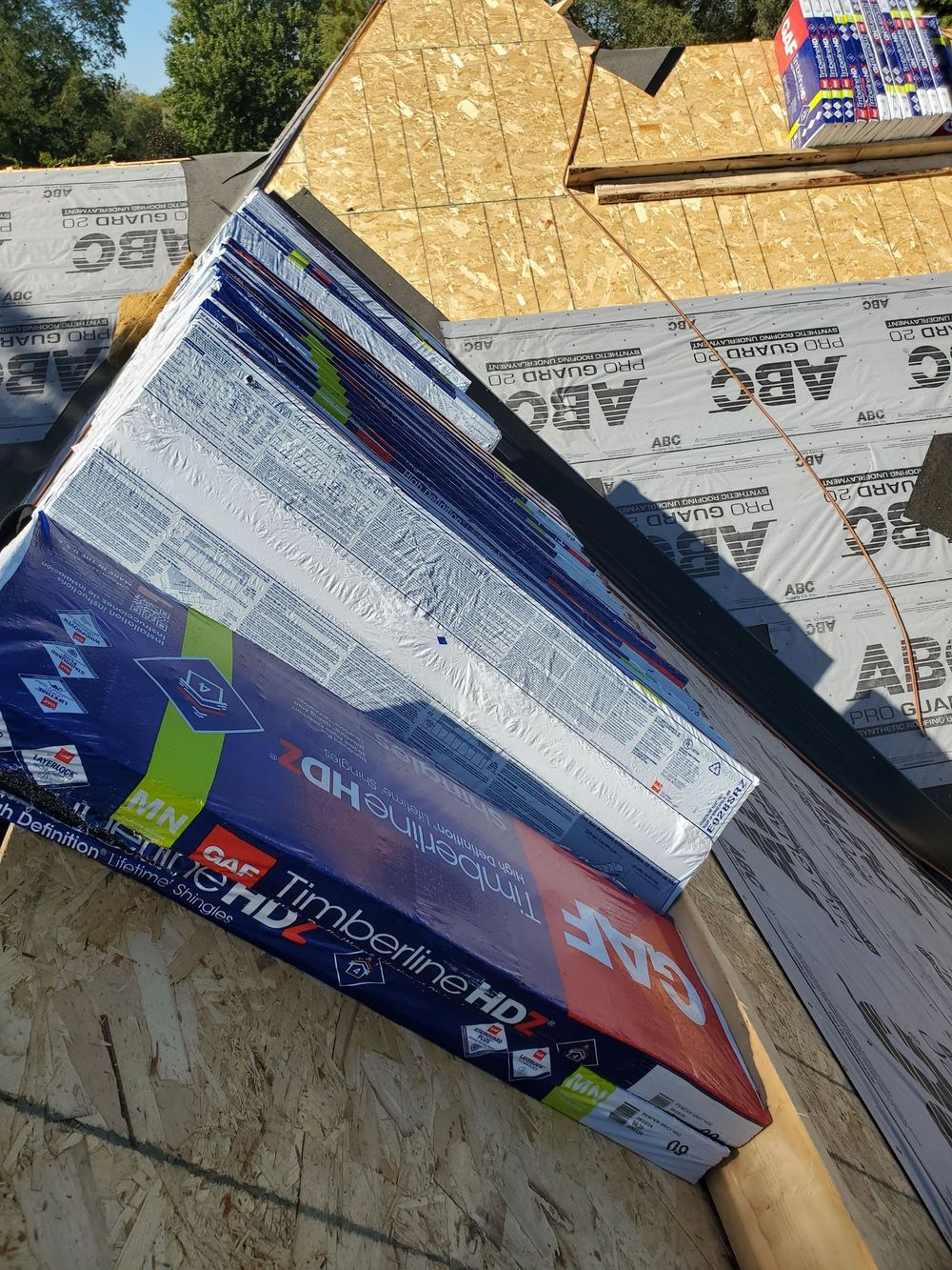 Bundles of GAF Timberline HDZ roofing shingles sit on a plywood roof deck covered in ABC underlayment.