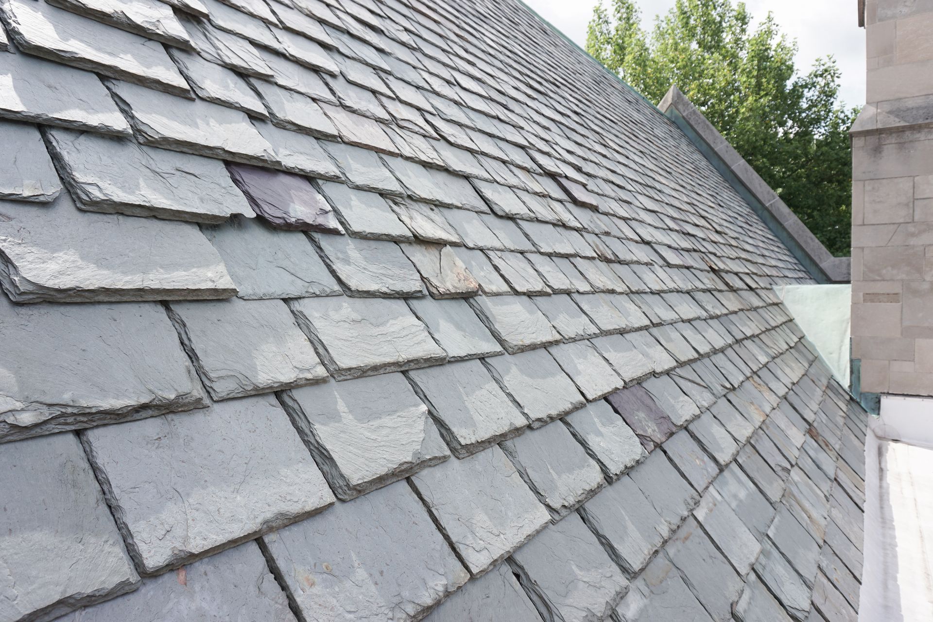 A sloped, shingled roof covered in light frost with a metal vent and a brick chimney under a cloudy sky.