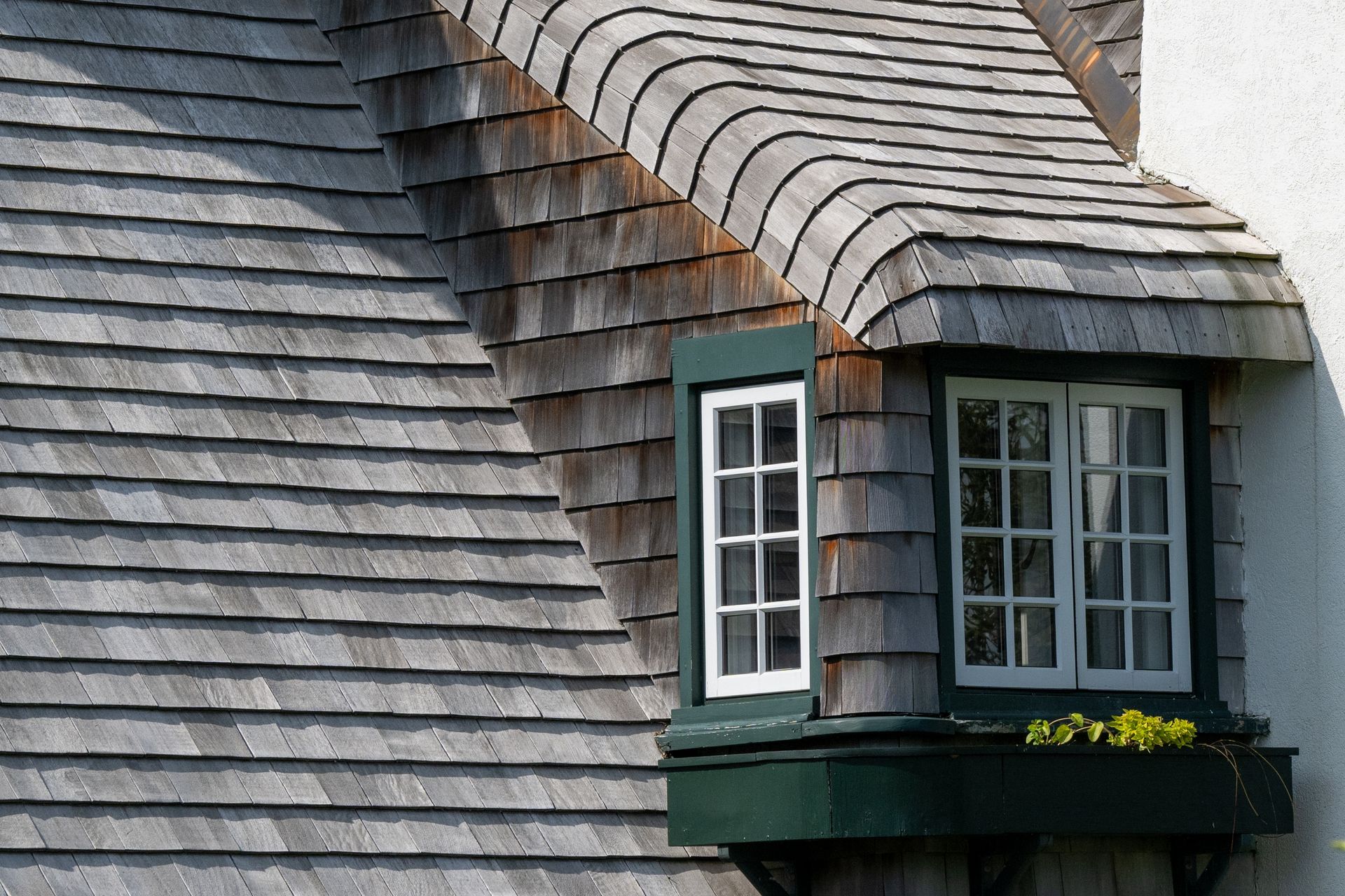 A weathered, shingled roof with a metal vent pipe and a brick chimney against a backdrop of bare tree branches.