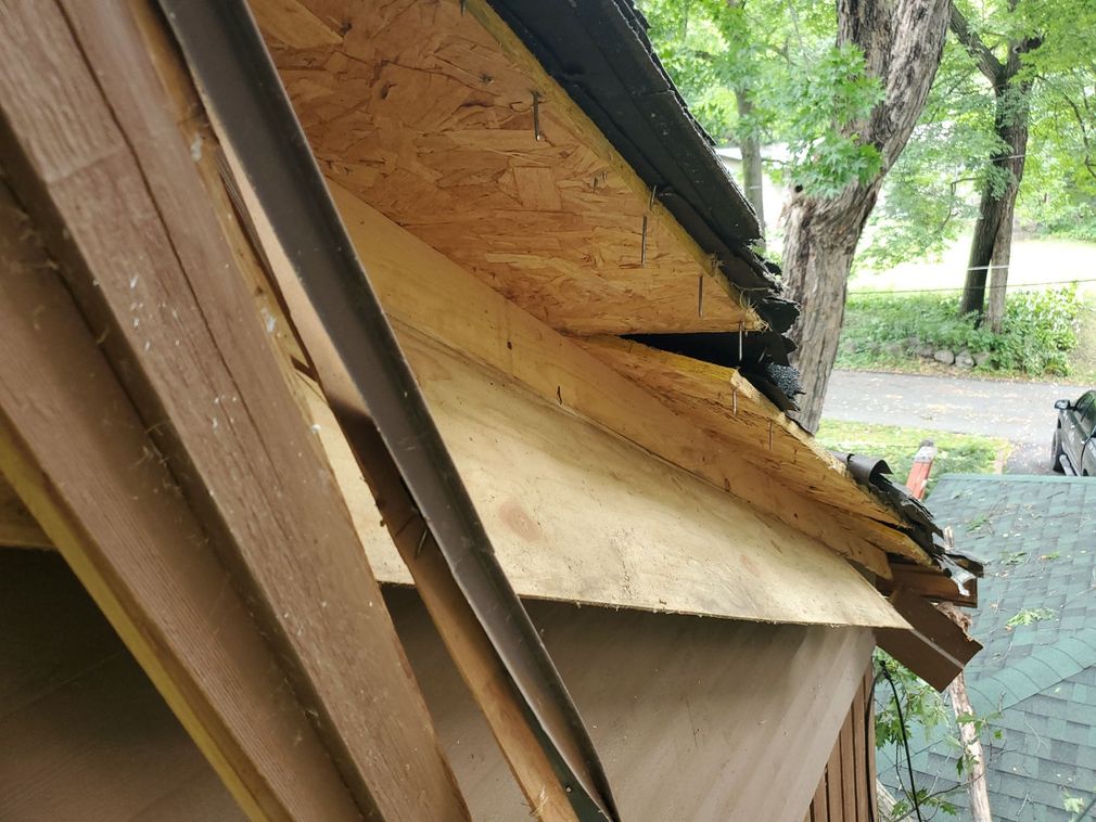 Close-up of a construction site showing new wooden roof sheathing being installed on a house frame near a tree.