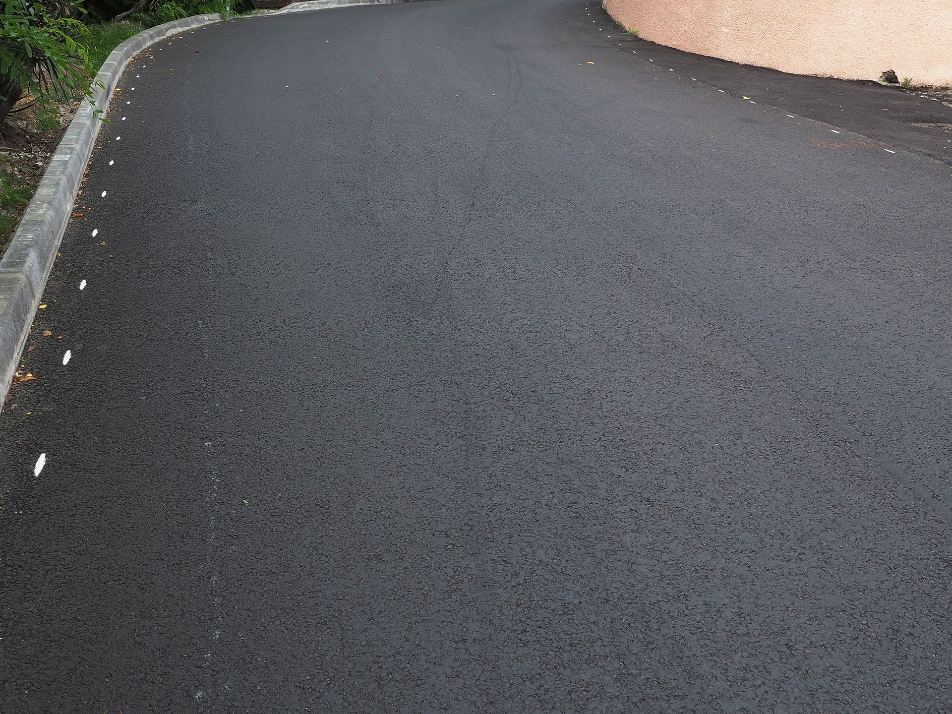 Black asphalt road curving to the right, bordered by a curb and building.