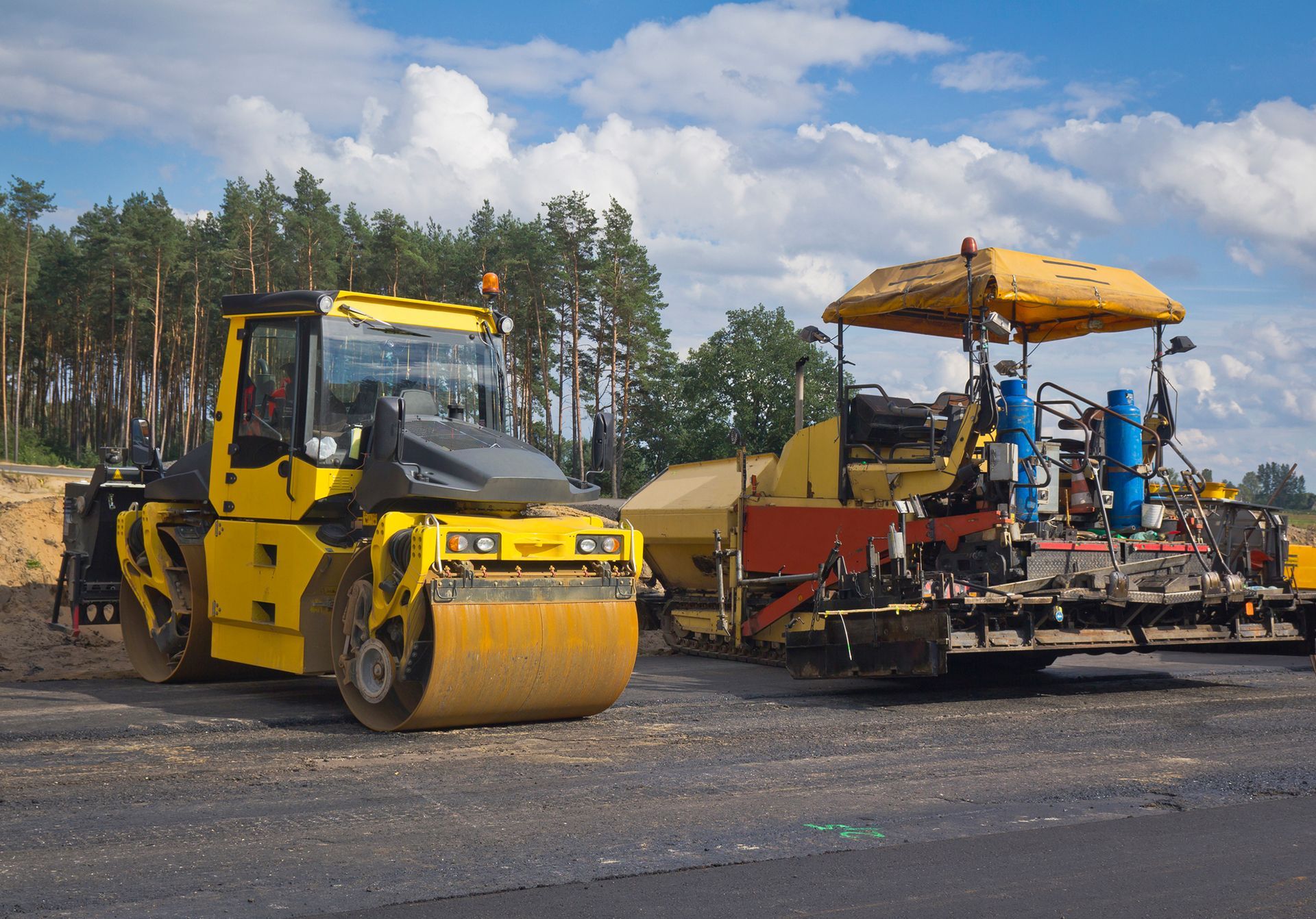Yellow road roller and paving machine on new asphalt, outdoors. Yellow road roller and paving machine on new asphalt, outdoors.