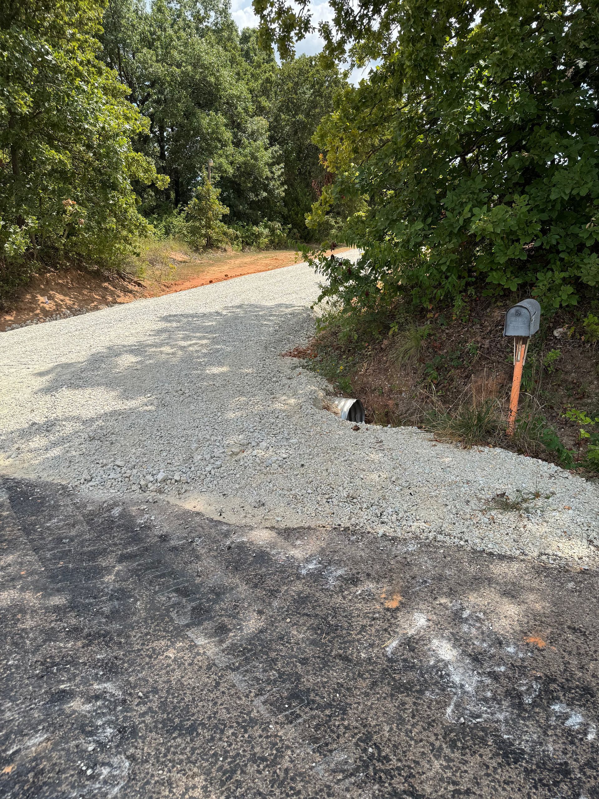 Gravel driveway transition from asphalt road; trees on both sides.