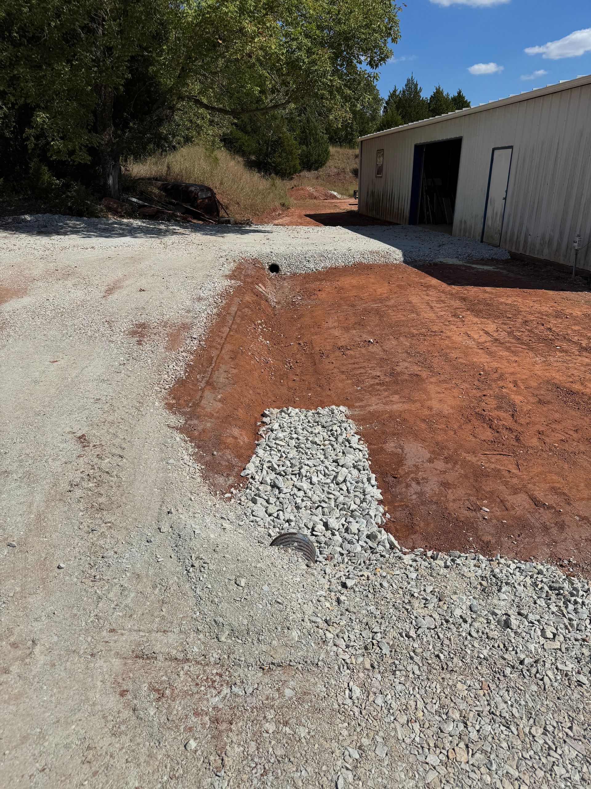 Gravel and red soil driveway leading to a white building. Construction in progress.
