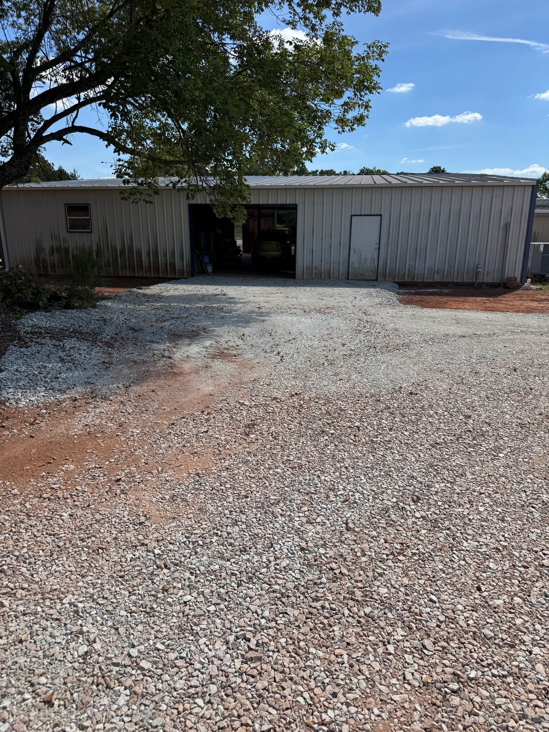 A weathered metal building with a gravel parking area under a bright blue sky.