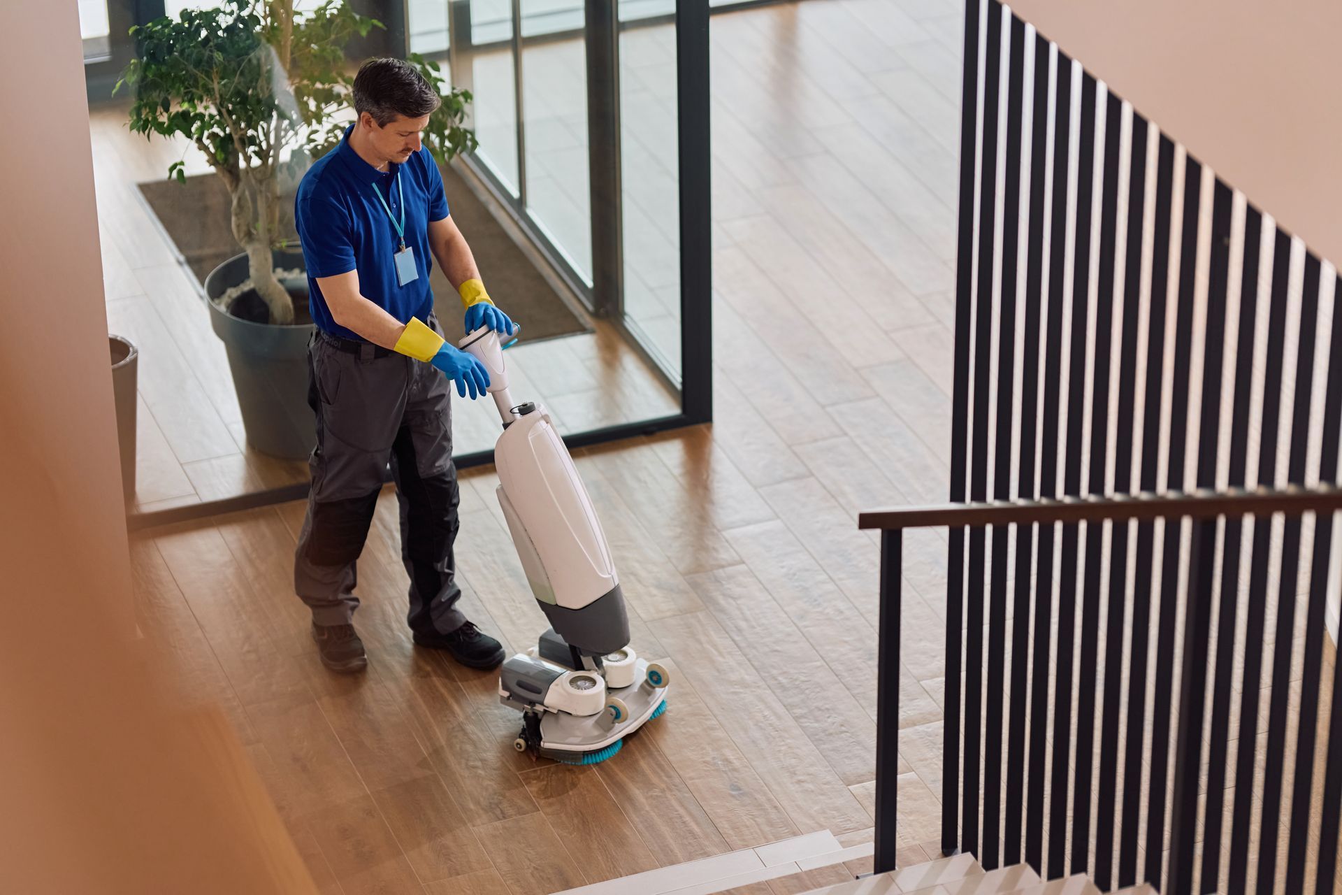 Person operating a floor polisher on a hardwood staircase landing indoors