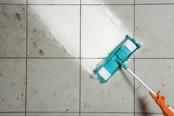 Person mopping a tiled floor with a teal mop head and orange handle