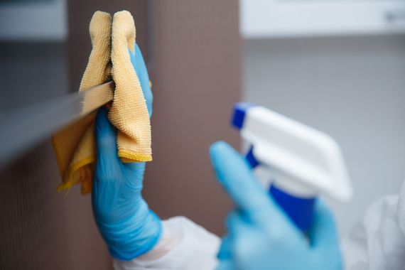Person wiping a coffee table with a blue cloth and spray cleaner in a living room