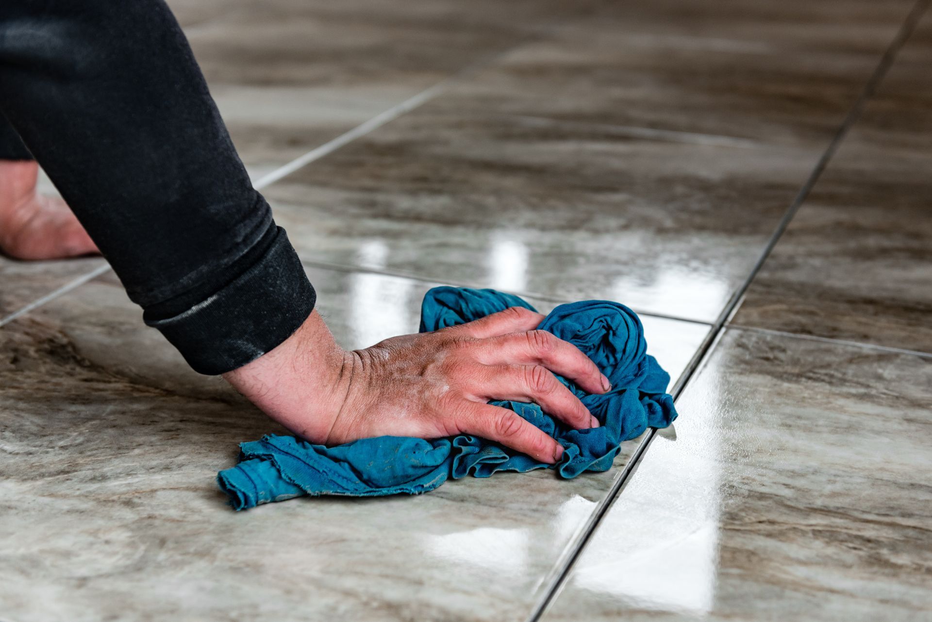 Hand wiping a tiled floor with a blue cloth Hand wiping a tiled floor with a blue cloth
