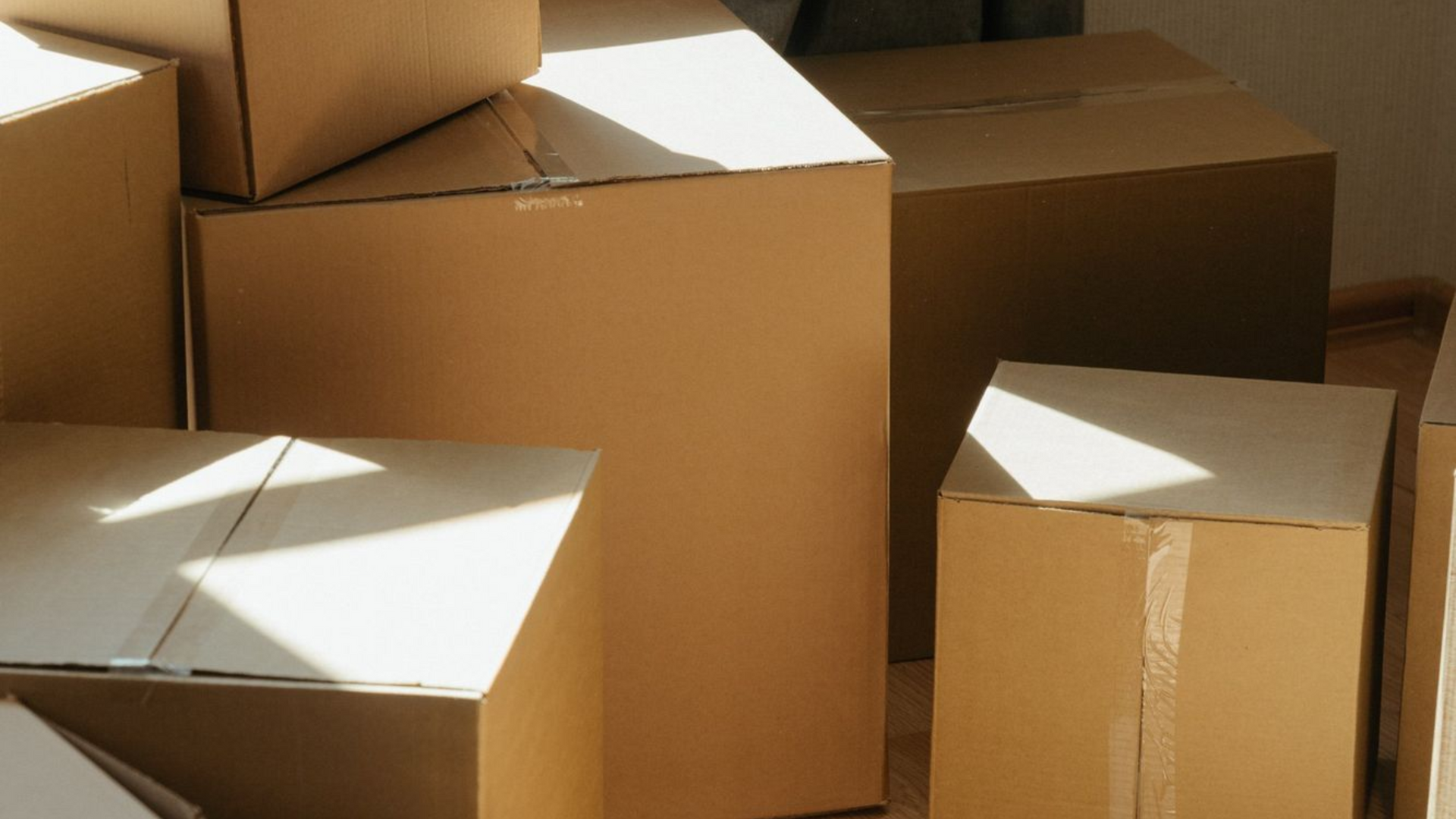 Stacked cardboard boxes with some open, lit by sunlight on a floor