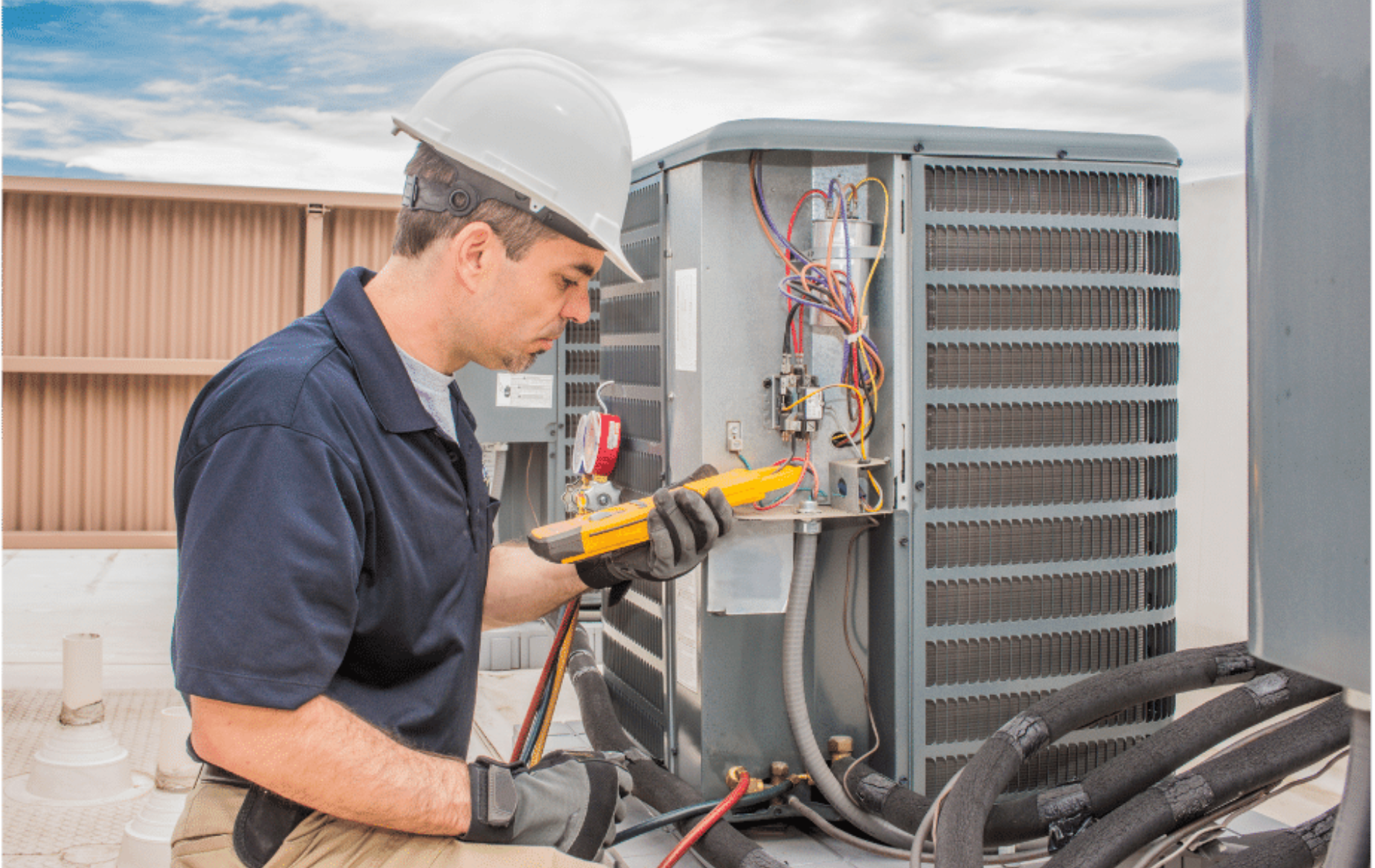 Technician in hard hat using a tool to service an outdoor HVAC unit with exposed wiring