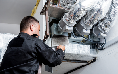 Technician inspecting ductwork and insulation inside a building ceiling