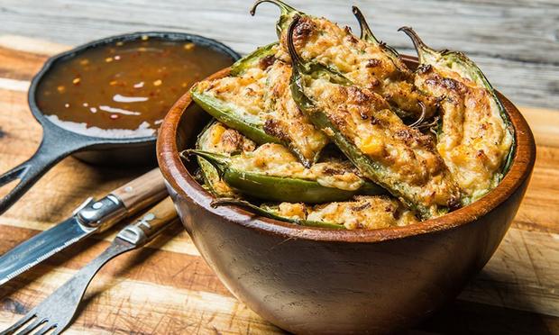 A bowl of stuffed peppers next to a pan of sauce on a wooden table.