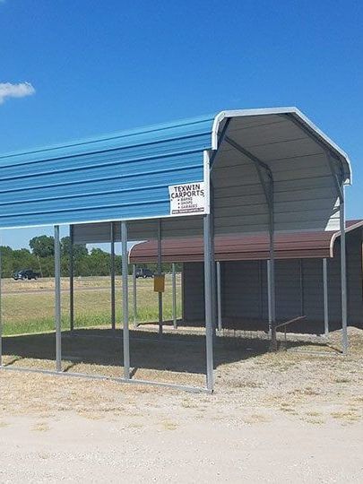 Blue-roofed metal shelter with open sides on a gravel lot under a clear sky