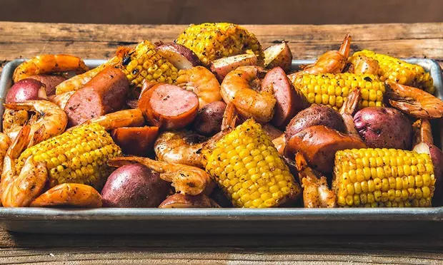 A tray of shrimp , corn , potatoes and sausage on a wooden table.