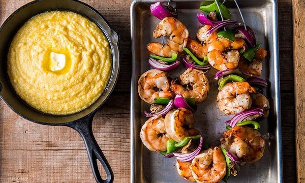 A pan of polenta next to a pan of shrimp on skewers.