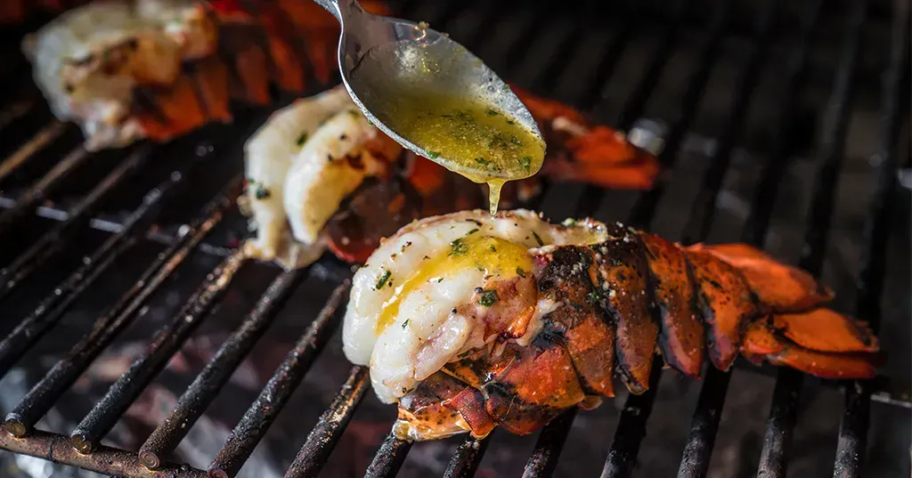 a lobster is being cooked on a grill with a spoon .