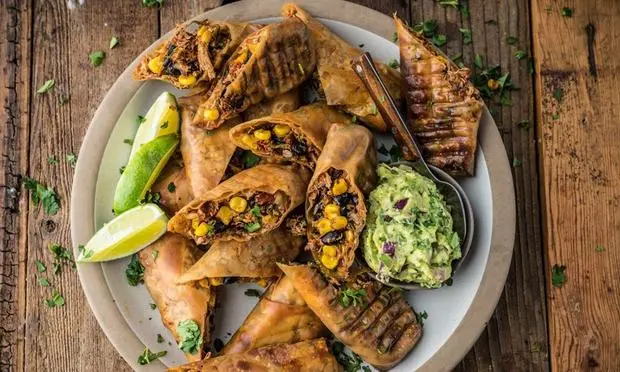 A plate of food with guacamole and lime wedges on a wooden table.