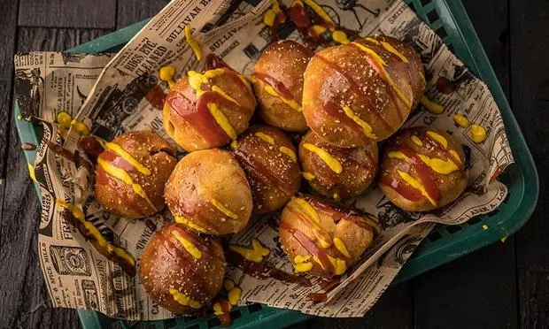 A bunch of hot dogs covered in ketchup and mustard on a tray.
