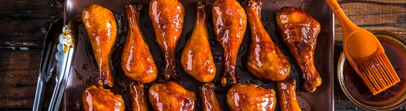 Chicken legs are being cooked in a pan with a brush and sauce.