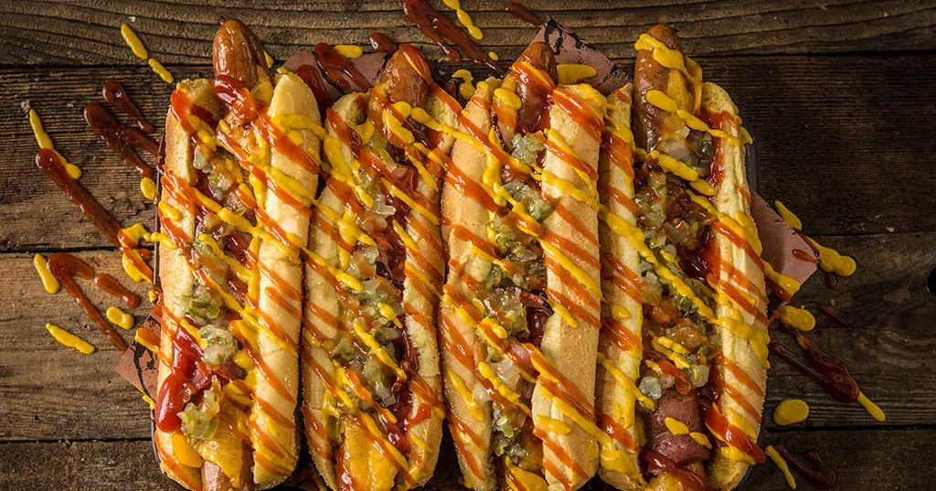 A bunch of hot dogs with ketchup and mustard on a wooden table.