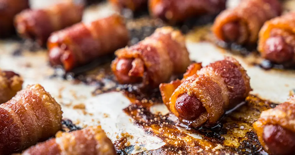 A bunch of bacon wrapped hot dogs are sitting on a table.