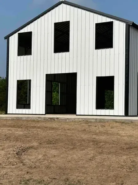 White two-story metal building with black-trimmed windows on a dirt lot