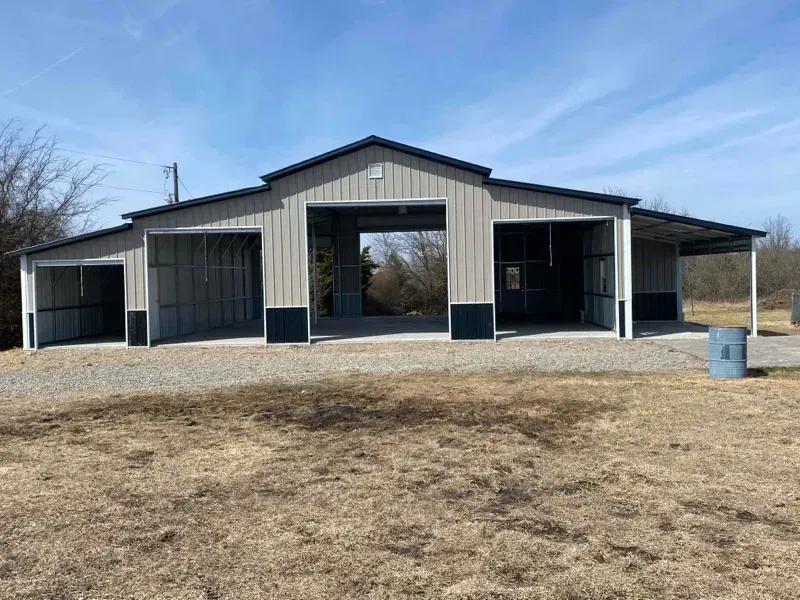 Large metal barn with open bays on a dry, grassy lot under a blue sky