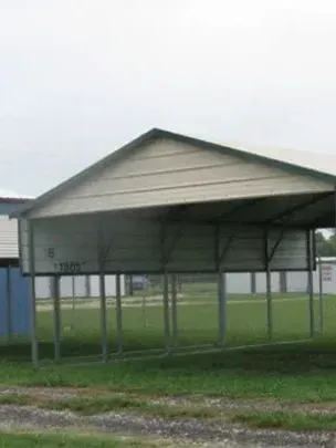 Small open-sided metal shelter with a sloped roof on a grassy field near a gravel path.