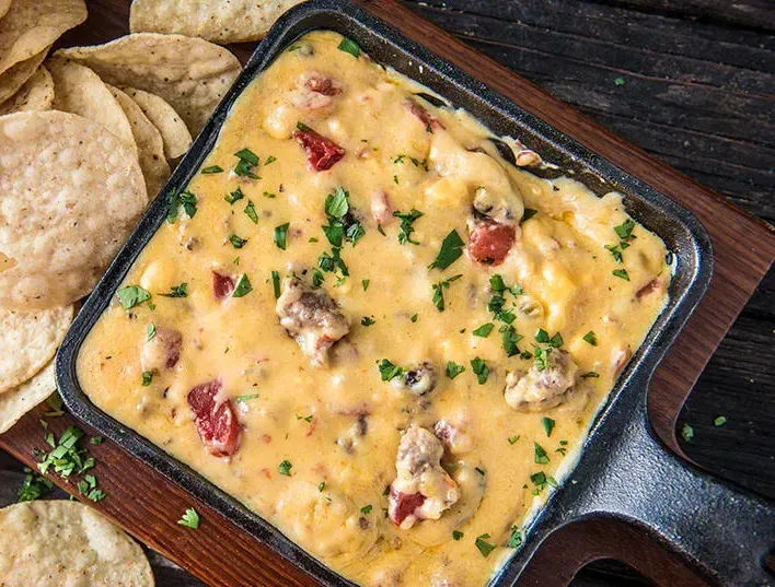 A pan of queso dip with tortilla chips on a wooden table.