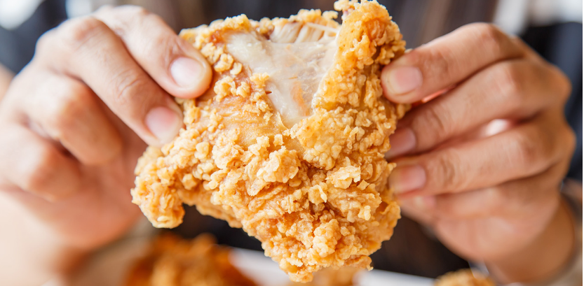 A person is holding a piece of fried chicken in their hands.
