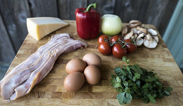 A wooden cutting board topped with eggs , bacon , peppers , tomatoes , mushrooms and cheese.