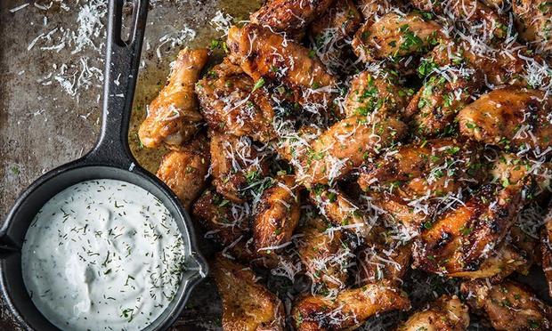 A skillet filled with chicken wings next to a bowl of ranch dressing.