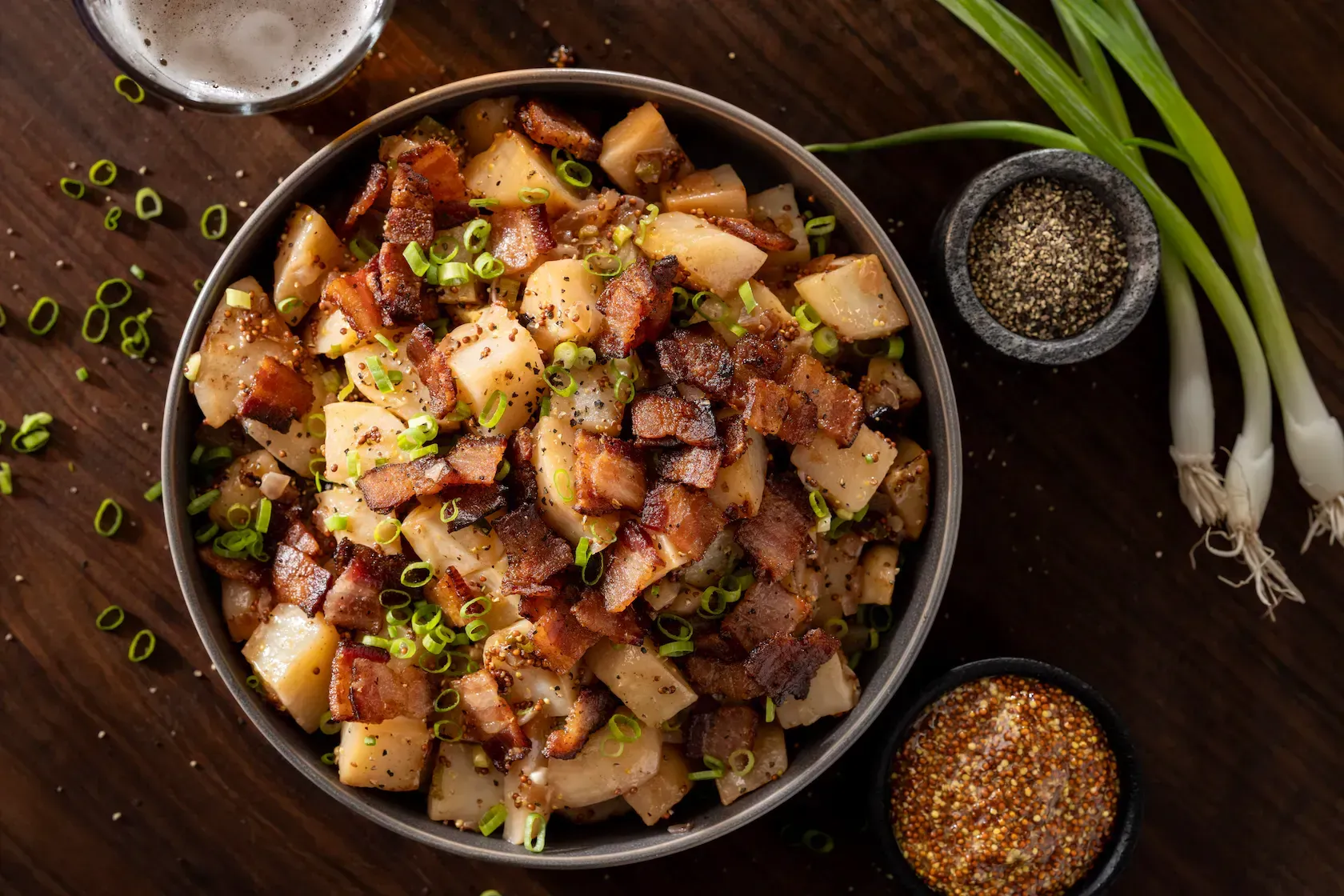 A bowl of potatoes with bacon and green onions on a wooden table.