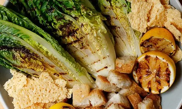 A close up of a plate of food with lettuce , chicken , lemons and crackers.