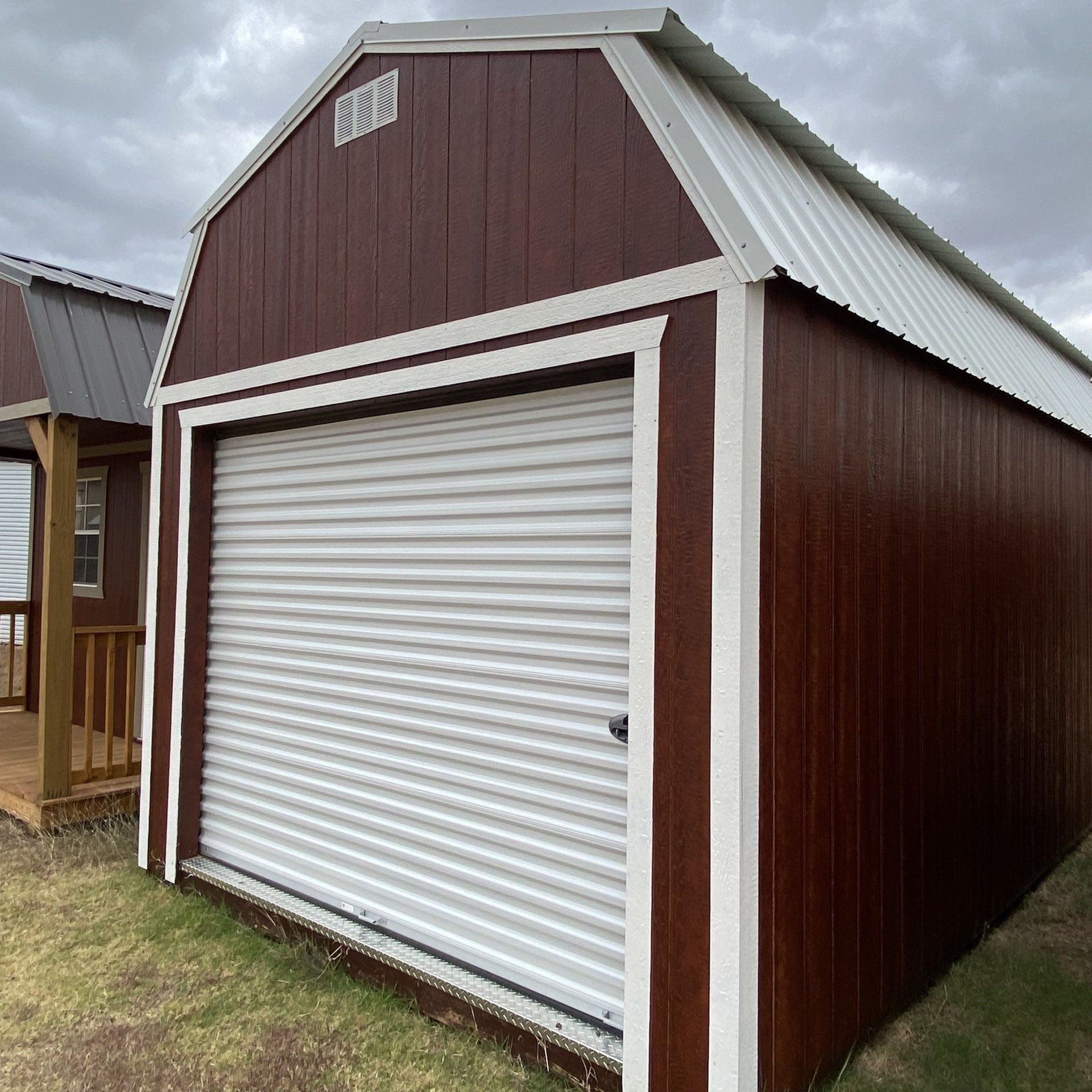 A brown barn with a white door is sitting on top of a lush green field.
