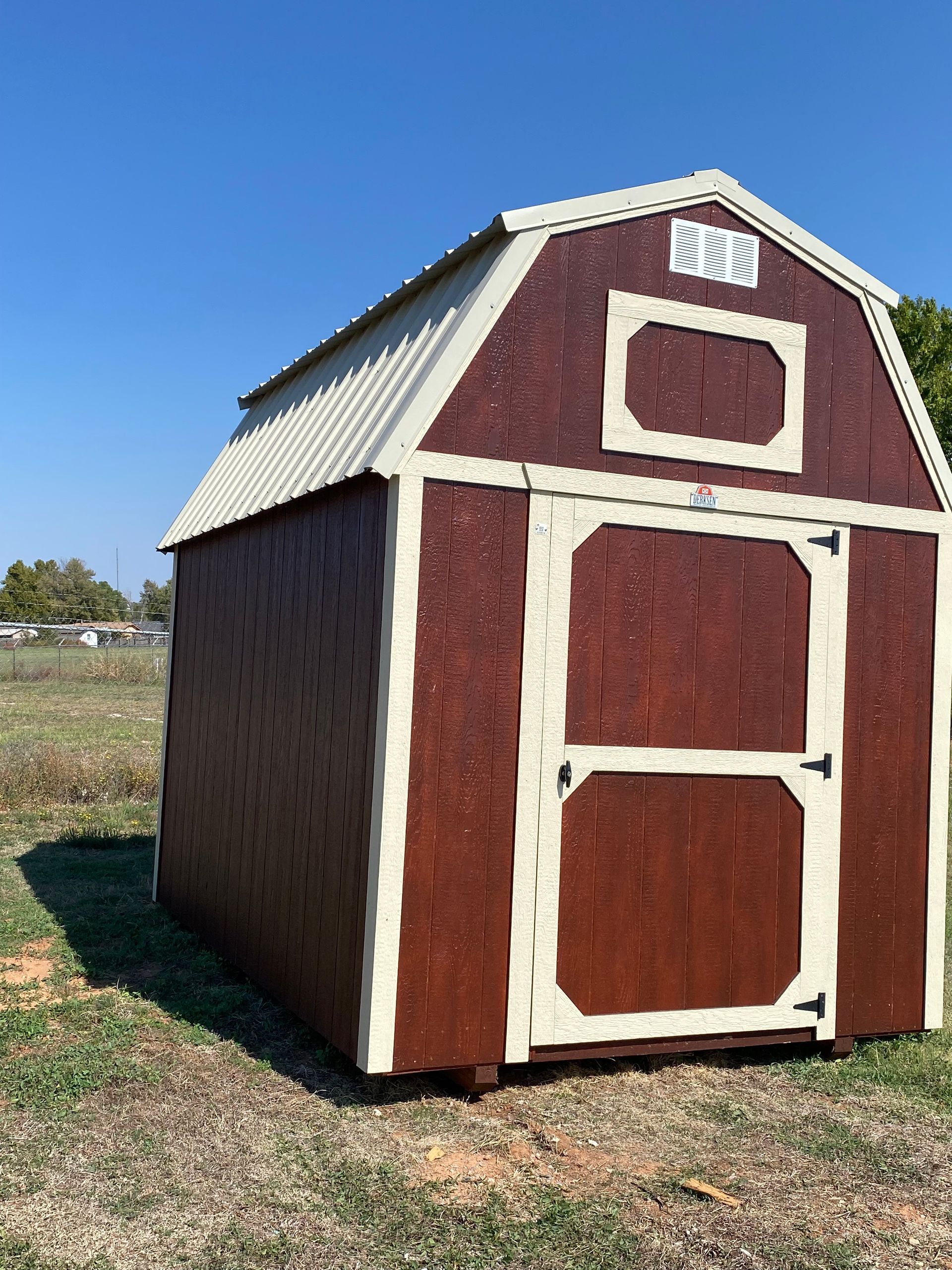 A shed with an ash gray siding a charcoal roof and charcoal trim with a double barn door is sitting in the middle of a field.