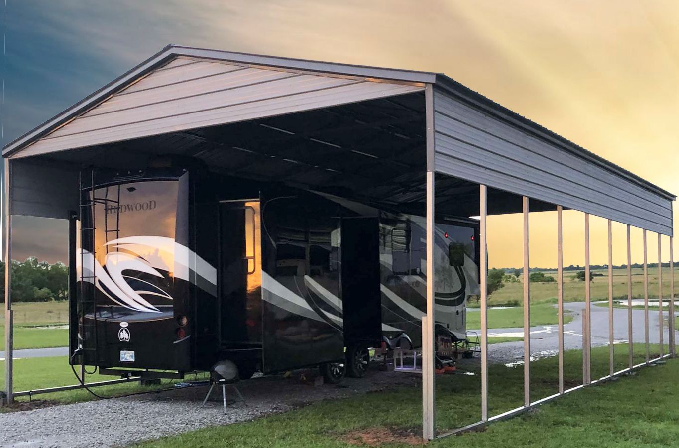 RV parked under a metal carport in a grassy rural area