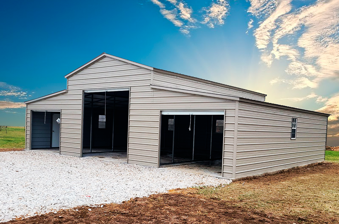 a large metal barn with two garage doors is sitting on top of a gravel driveway .