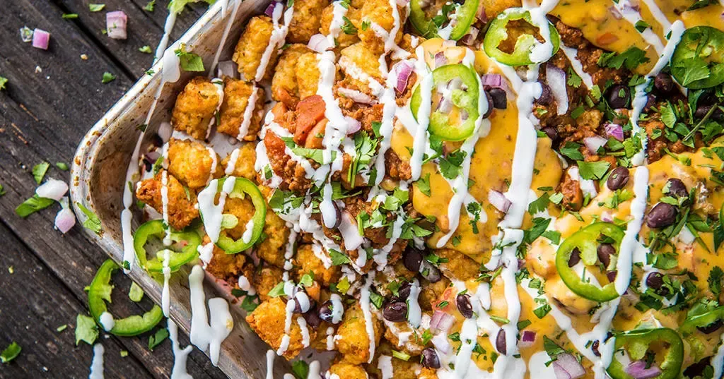 A close up of a tray of nachos on a wooden table.