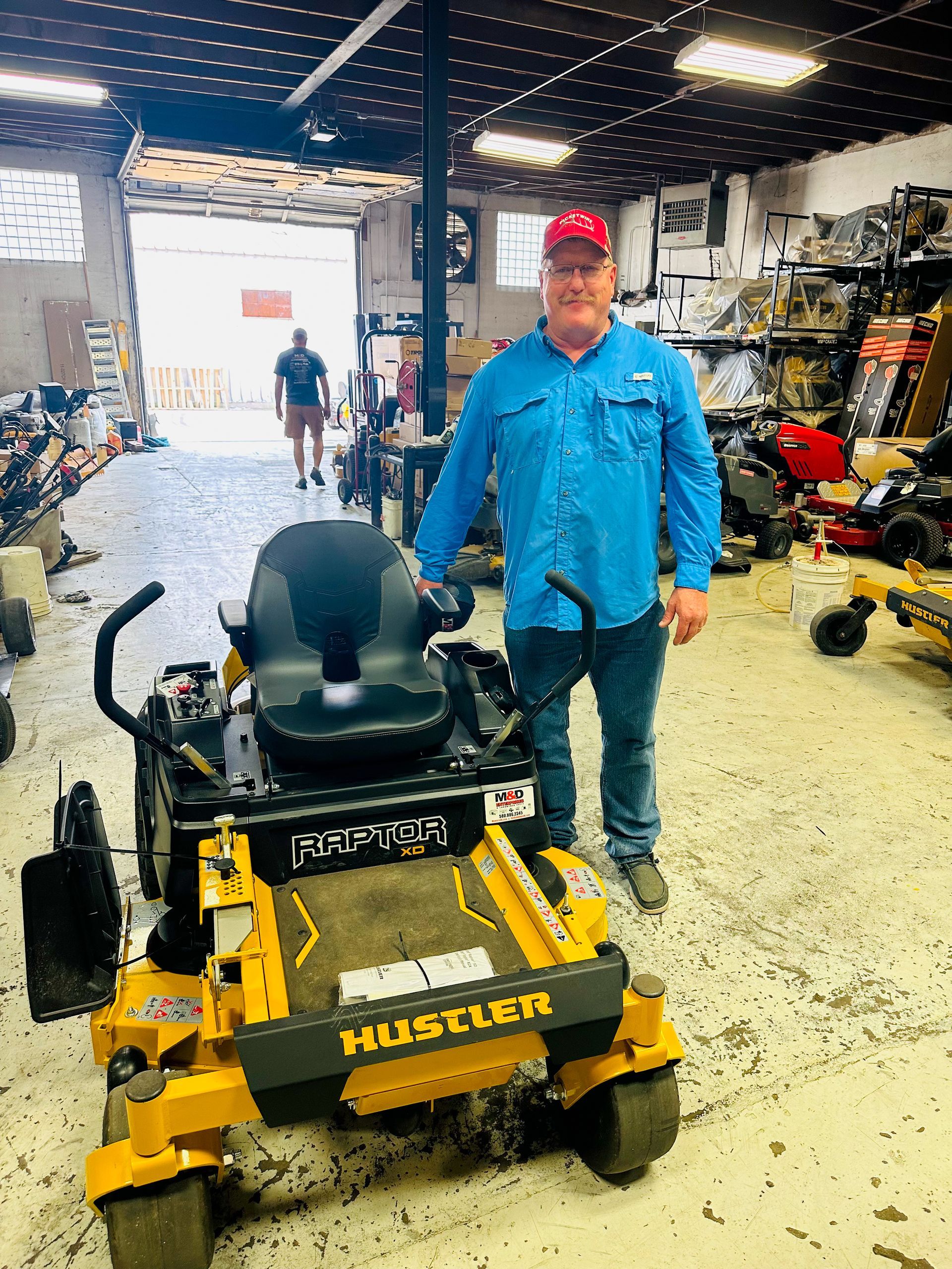 Un hombre está parado frente a una cortadora de césped Husqvarna en un garaje.